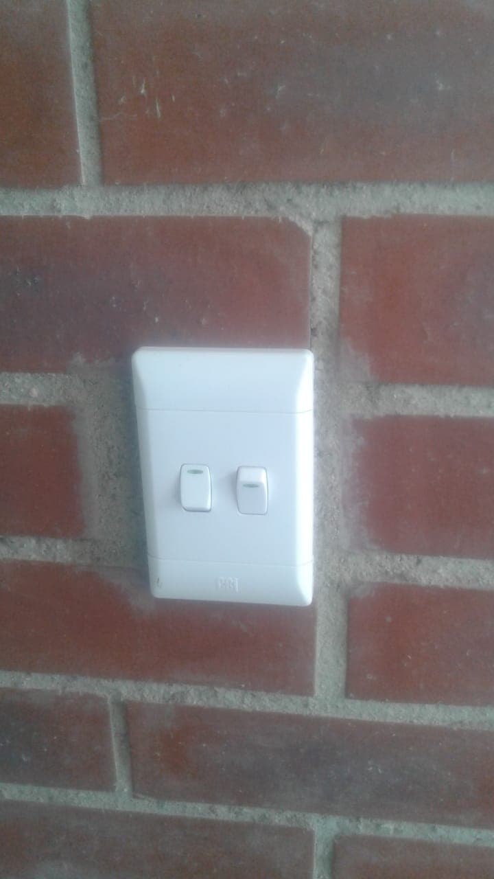 White double light switch mounted on a red brick wall