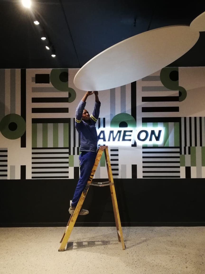 Electrician on a ladder installing a circular ceiling light in a commercial interior