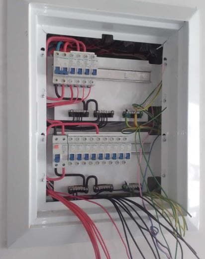 Wall-mounted distribution board with two rows of circuit breakers and earth wiring visible
