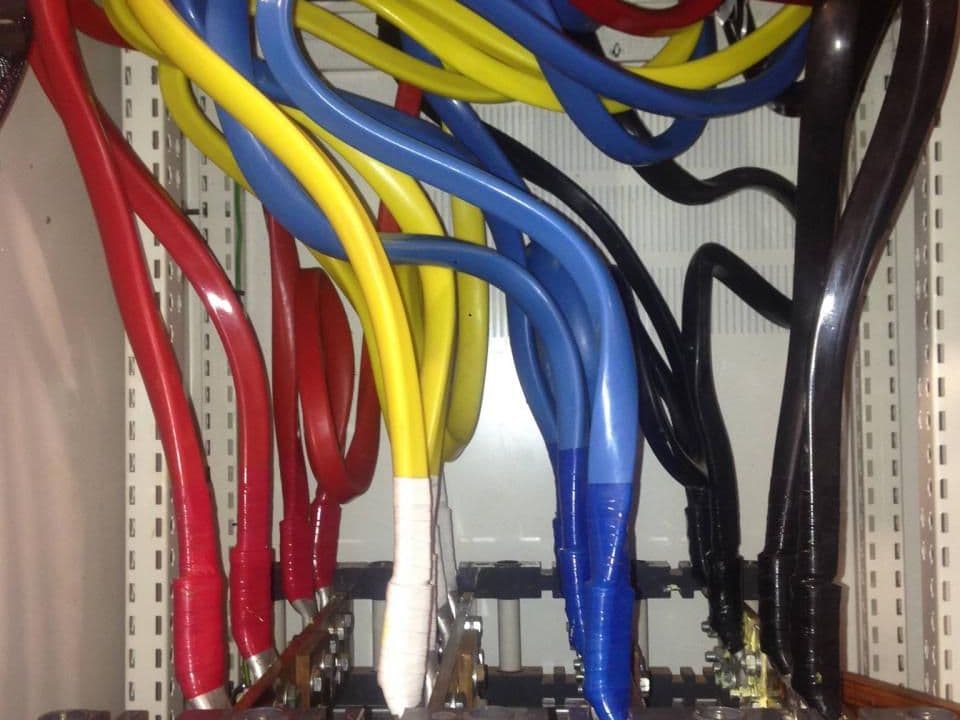 Heavy-duty red, yellow, blue and black cables terminated onto copper busbars inside a metal enclosure